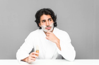 Sakalını kesen genç adam şüpheli ve şüpheci bir ifadeyle yana bakıyor..