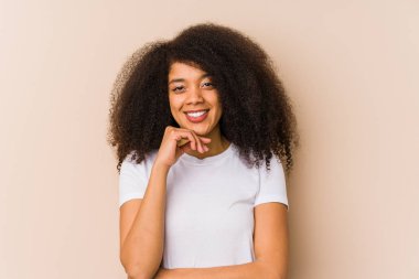 Genç Afrikalı Amerikalı kadın gülümsüyor mutlu ve kendinden emin, elleriyle çenesine dokunuyor..