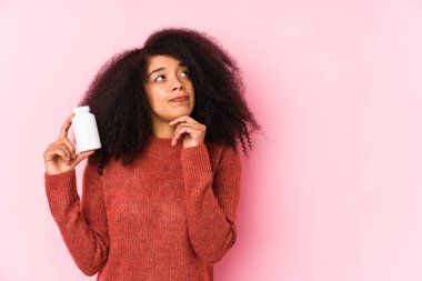 Vitaminlerini tutan genç afro kadın şüpheli ve şüpheci bir ifadeyle vitaminlere bakan genç bir afro kadını izole etti..