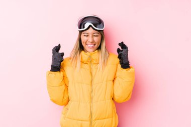 Pembe arka planda kayak kıyafeti giyen beyaz bir kadın şans getirsin diye dua ediyor.