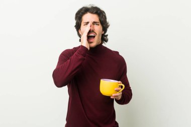 Young caucasian man holding a coffee cup shouting excited to front.