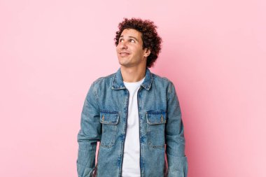 Pembe arka planda kot ceket giyen kıvırcık, olgun bir adam amaçlarına ve amaçlarına ulaşma hayali kuruyor.