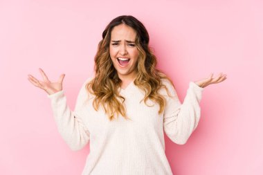 Pembe arka planda poz veren kıvrımlı genç kadın öfkeyle bağırıyor..