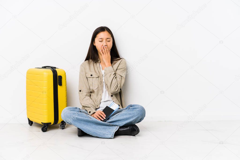 Young chinese traveler woman sitting holding a boarding passes yawning showing a tired gesture covering mouth with hand.
