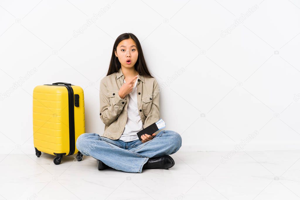 Young chinese traveler woman sitting holding a boarding passes pointing to the side