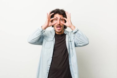 Young handsome man against a white background keeping eyes opened to find a success opportunity.