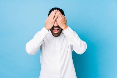 Mavi arka planda genç bir latin adam. Gözlerinizi ellerinizle kapayın. Gülümseyin ve bir sürpriz bekleyin..