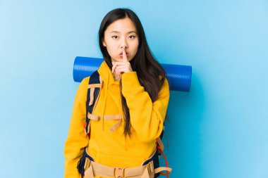Young chinese backpacker woman isolated keeping a secret or asking for silence.