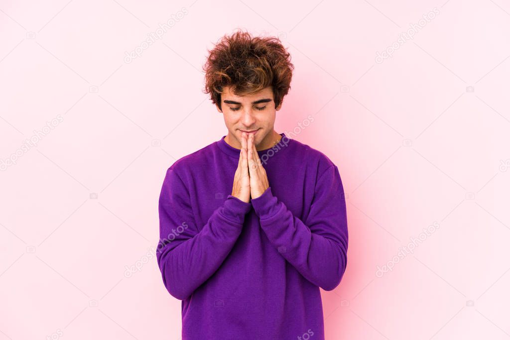 Young caucasian man against a pink background isolated holding hands in pray near mouth, feels confident.