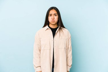 Mavi arka planda izole edilmiş genç bir kadın yanakları patlatıyor, yorgun bir ifade takınıyor. Yüz ifadesi kavramı.