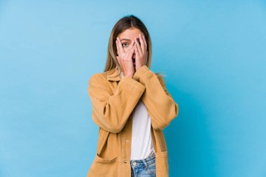 Genç beyaz kadın parmaklarının arasından korkmuş ve gergin bir şekilde göz kırpıyor..