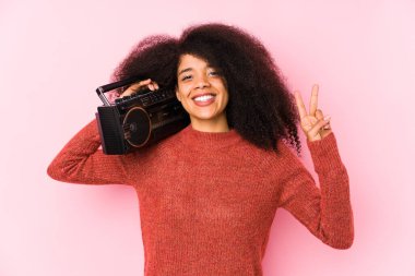 Genç Afro kadın, elinde bir kaset tutuyor. İki numarayı parmaklarıyla gösteriyor..