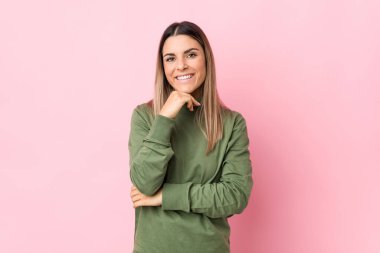 Kafkasyalı genç bir kadın yalnız, mutlu ve kendinden emin gülümsüyor, elleriyle çenesine dokunuyor..