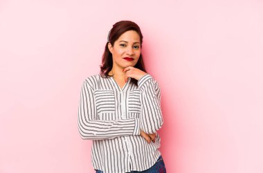 Orta yaşlı Latin bir kadın pembe bir arka planda izole edilmiş mutlu ve kendinden emin gülümsüyor, elleriyle çenesine dokunuyor..