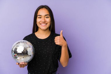 Genç Asyalı bir kadın bir balo düzenliyor yalnız, gülümsüyor ve başparmağını kaldırıyor.