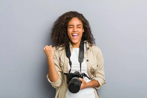若いアフリカ系アメリカ人の写真家の女性が気楽で興奮したカメラを持っている 勝利のコンセプト — ストック写真