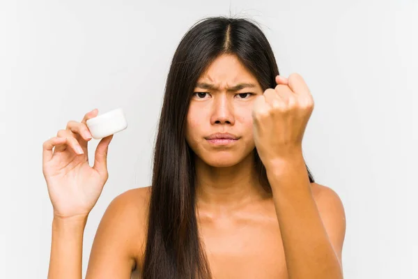 年轻的中国女人拿着保湿霜隔离显示拳头对相机 侵略性的面部表情 — 图库照片