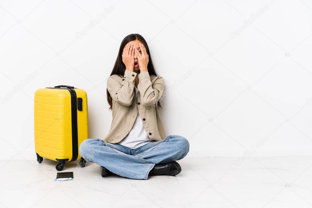 Young chinese traveler woman sitting holding a boarding passes blink through fingers frightened and nervous.