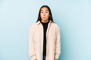 Mavi arka planda izole edilmiş genç bir kadın omuzlarını silker ve gözleri açık kalır..