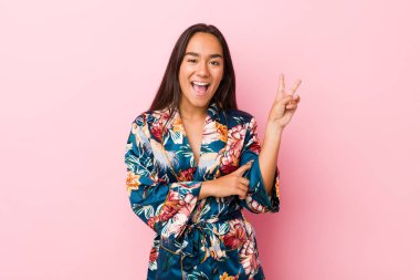 Kimono pijama giyen genç Hintli kadın neşeli ve tasasız parmaklarıyla barış sembolü gösteriyor..