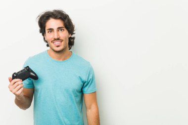 Bir oyun denetleyicisi tutan genç adam çapraz kolları ile kendinden emin gülümseyen.