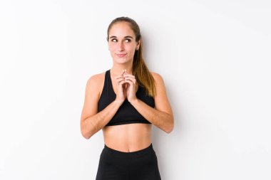 Beyaz arka planda poz veren Kafkasyalı genç bir fitness kadını. Kafasında bir plan kuruyor..