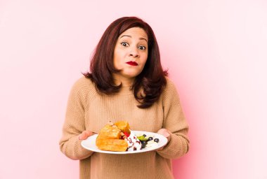 Orta yaşlı, waffle tutan, omuz silken, gözleri açık bir Latin kadın..