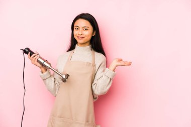Genç Çinli bir kadın mikser tutuyor. İzole edilmiş, rahat bir şekilde fotokopi odasına bakan bir şey düşünüyor..