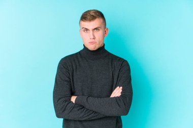 Mavi arka planda genç, beyaz bir adam kameraya alaycı bir ifadeyle bakıyor..