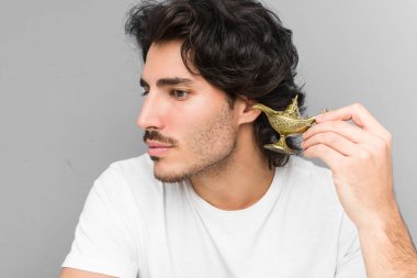 Gri bir arka planda izole edilmiş sihirli bir lamba tutan genç beyaz bir adam.