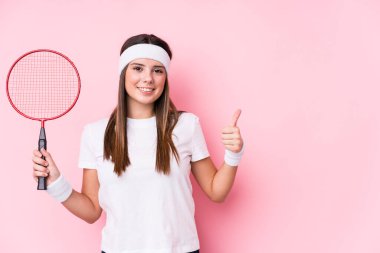 Badminton oynayan beyaz bir kadın kendini izole edip gülümsüyor ve başparmağını kaldırıyor.