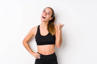 Beyaz arka planda poz veren beyaz tenli kadın başparmak uzakta, gülüyor ve kaygısız..