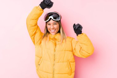 Young caucasian woman wearing a ski clothes in a pink background celebrating a special day, jumps and raise arms with energy.