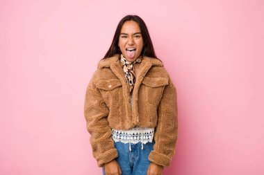 Young mixed race indian woman wearing a short sheepskin coatfunny and friendly sticking out tongue.