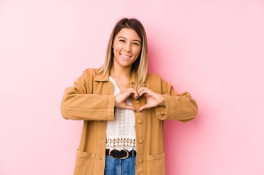 Kafkasyalı genç bir kadın yalnız poz veriyor gülümsüyor ve elleriyle kalp şeklini gösteriyor..