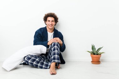 Olgun bir adam pijamasını giymiş, yerde mutlu, gülümseyen ve neşeli bir şekilde oturuyor..