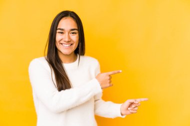 Sarı arka planda izole edilmiş genç bir kadın işaret parmağıyla işaret ederek heyecanlanıyor..