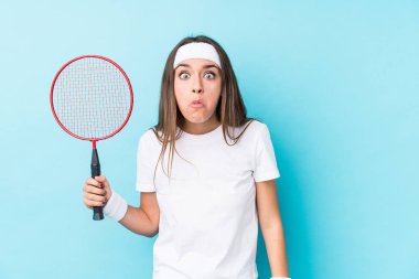 Badminton oynayan beyaz bir kadın omuz silkiyor ve gözleri açık..