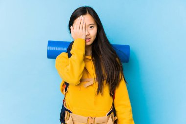 Young chinese backpacker woman isolated having fun covering half of face with palm.