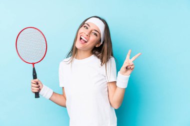 Badminton oynayan beyaz bir kadın neşeli ve tasasız bir şekilde parmaklarıyla barış sembolü gösteriyor..