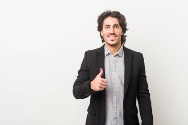 Beyaz bir geçmişi olan genç bir iş adamı gülümsüyor ve başparmağını kaldırıyor.