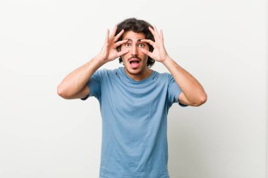 Young handsome man against a white background keeping eyes opened to find a success opportunity.