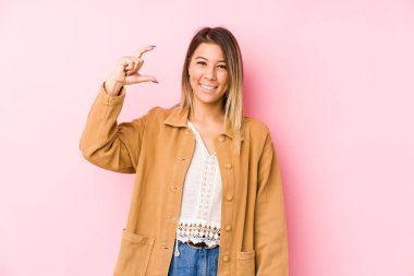 Kafkasyalı genç bir kadın yalnız poz veriyor, işaret parmaklarıyla küçük bir şey tutuyor, gülümsüyor ve kendinden emin..