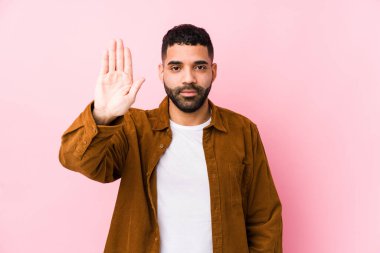 Pembe arka planı olan genç bir latin adam elini uzatmış, dur işareti gösteriyor ve seni engelliyor..