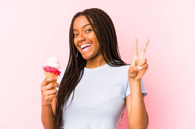 Genç Afrikalı Amerikalı bir kadın dondurma tutuyor neşeli ve tasasız bir şekilde parmaklarıyla barış sembolü gösteriyor..