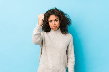 Genç Afro-Amerikan kıvırcık saçlı kadın kameraya yumruğunu gösteriyor, agresif yüz ifadesi..