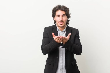 Genç iş adamı beyaz arka planda dudakları kıvrılmış ve avuç içleriyle hava öpücüğü yolluyor..