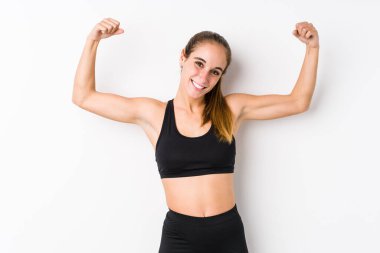 Young caucasian fitness woman posing in a white background showing strength gesture with arms, symbol of feminine power