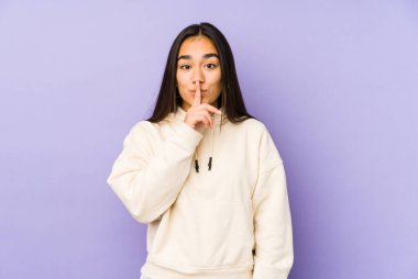 Young woman isolated on a purple background keeping a secret or asking for silence.
