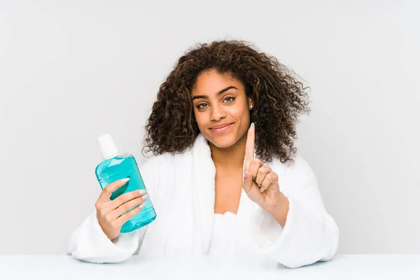 Young african american woman holding a mouth wash showing number one with finger.
